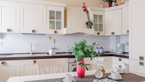 A kitchen with white cabinets, a sink, a stove, and a dining table set with cups and a vase of flowers. - Italian Experience- Sweet Loreto (Loreto)
