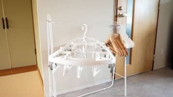 A white drying rack with multiple hangers and a wooden hanger in a room with beige walls and a wooden door.