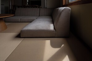 Een modulaire bank, een ronde houten tafel en een geweven vloermat in een kamer met een raam.
