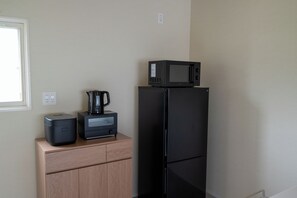 Una cocina con un refrigerador negro, un microondas encima, una cafetera y un mueble pequeño.