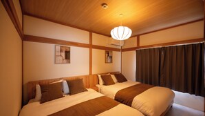 Ein Hotelzimmer mit zwei Betten, Holz-Kopfteilen, einer Deckenleuchte und einem fensterbelaubten Fenster.