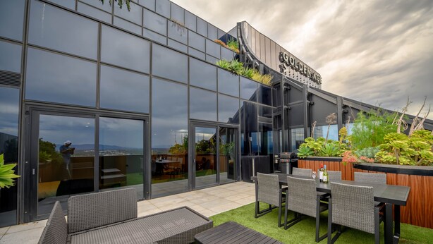 A modern building with a glass facade, outdoor seating area with wicker furniture, and a sign reading 'Golden Age.'