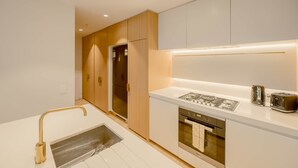 A modern kitchen with white cabinetry, stainless steel appliances, and a gold faucet.