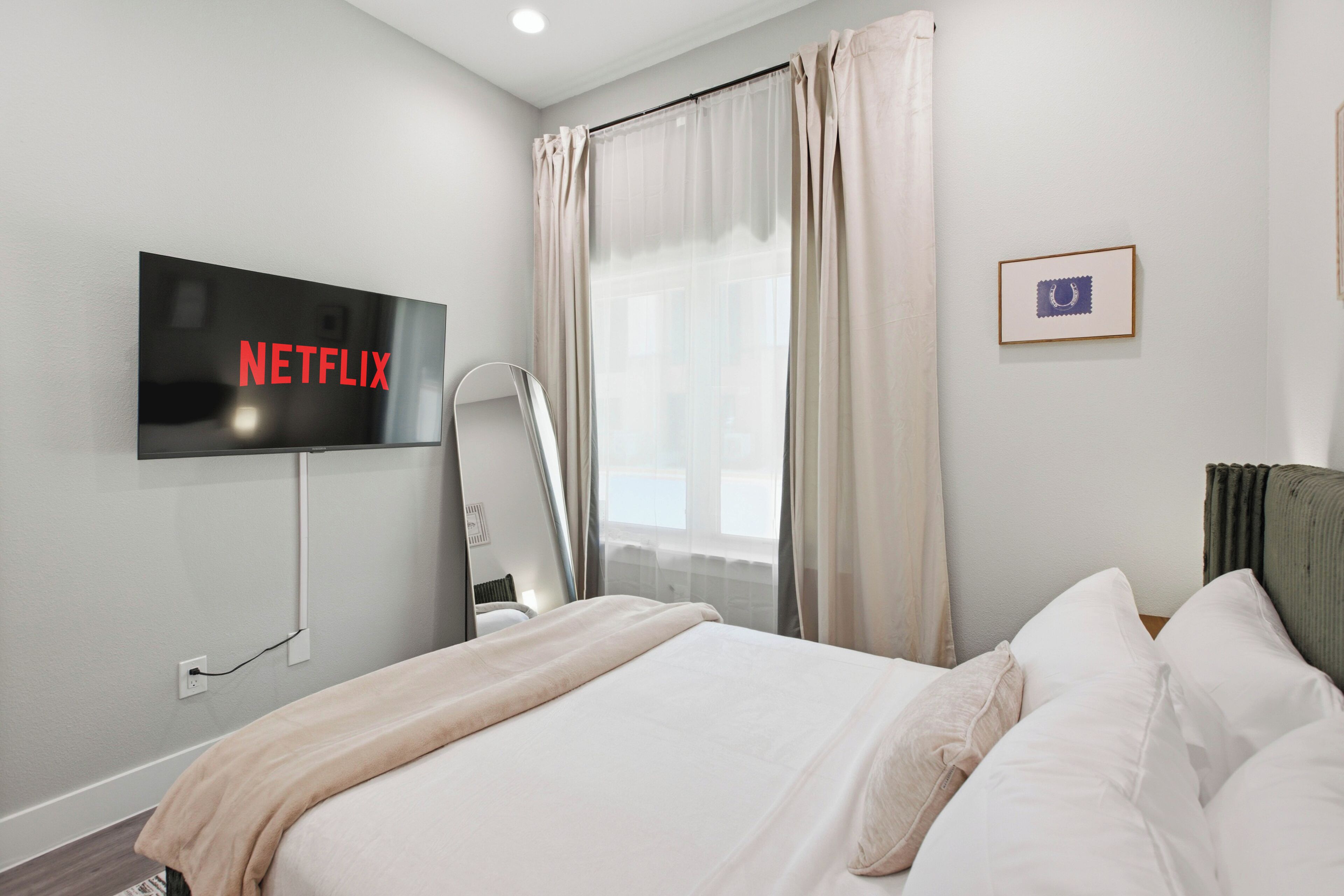 Een moderne hotelkamer met een bed, een aan de muur bevestigde televisie, een raam met gordijnen en een lijst met een foto aan de muur.