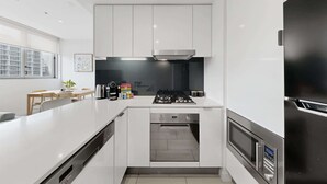 Una cocina moderna con armarios blancos, horno empotrado y refrigerador de acero inoxidable.