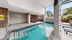 Una piscina interior con solárium alicatado, zona de estar y vistas de los edificios circundantes.