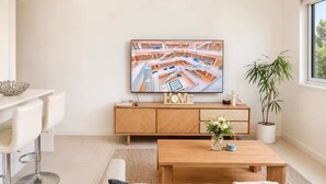 Una sala moderna con un sofá, una mesa de centro y un televisor montado en la pared mostrando un paisaje urbano.