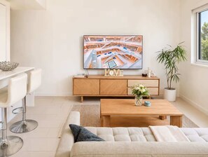 Ein modernes Wohnzimmer mit einer Couch, einem Couchtisch und einem an der Wand montierten Fernseher, der eine Stadtansicht zeigt.