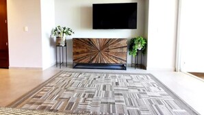 Ein modernes Wohnzimmer mit einem großen, gemusterten Teppich, einem Wand-Fernseher und zwei Blumentöpfen.