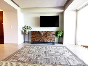 A modern living room with a large, patterned rug, a mounted TV, and two potted plants. - Harbor 171 | Oceanfront | Infinity Pools | Pet-Friendly (Puerto Vallarta)