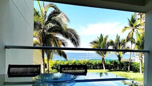 Ein Zimmer mit Glastisch und Stühlen, Blick aufs Meer und Palmen.