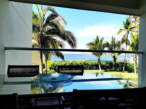 A room with a glass table and chairs, a view of the ocean, and palm trees. - Harbor 171 | Oceanfront | Infinity Pools | Pet-Friendly (Puerto Vallarta)