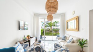Uma sala de estar moderna com sofá, cadeiras, mesa de jantar e uma grande janela com vista para palmeiras.