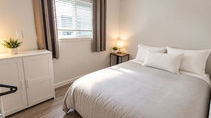 A bedroom with a bed, bedside table, lamp, potted plant, and a wardrobe. - Park view home (Vancouver)