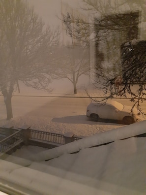Une rue enneigée, avec une voiture garée et des arbres sans feuilles.