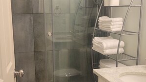 A bathroom with a glass-enclosed shower, a toilet, and a metal towel rack with folded towels. - Park view home (Vancouver)