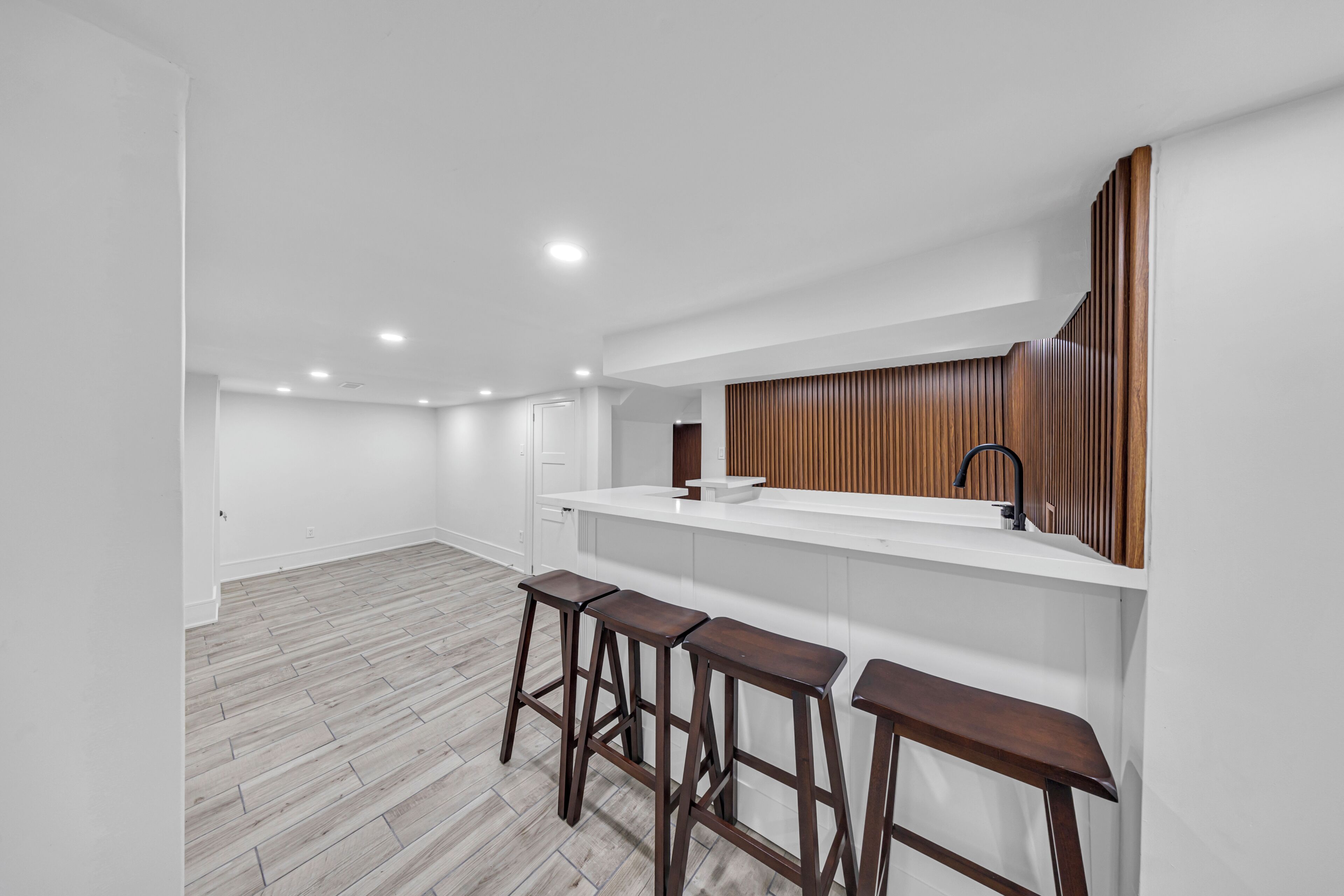 A modern kitchen with white cabinetry, a wooden accent wall, and a bar area with stools.