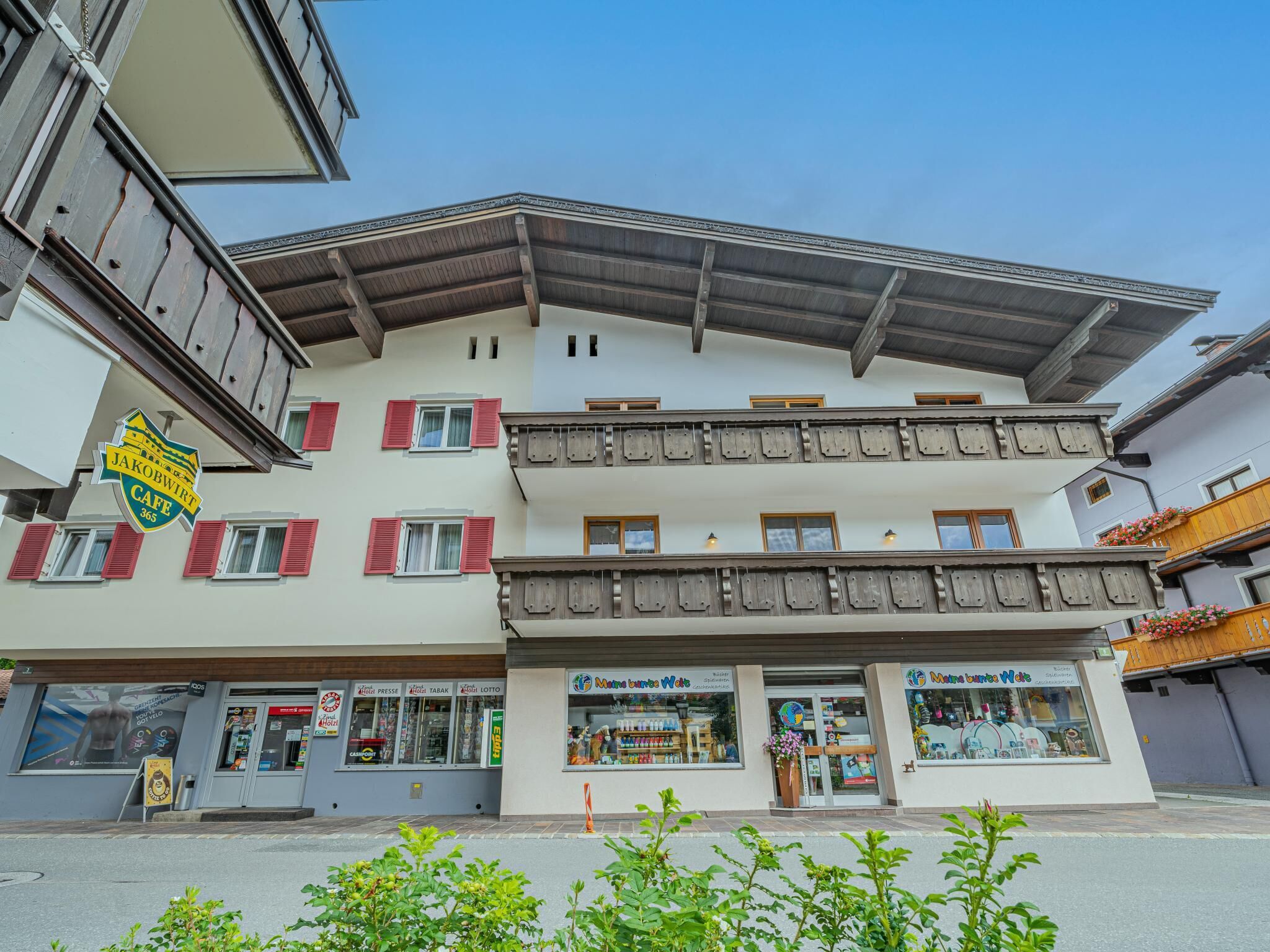 Un immeuble à plusieurs étages abritant au rez-de-chaussée un café appelé « Jakobwirt », une pharmacie et un magasin dont l’enseigne est colorée.
