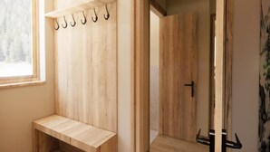 Een houten kleedruimte met een bankje, haken en een deur naar een andere kamer.
