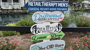 Ein Wegweiser mit verschiedenen Geschäftsnamen, darunter 'Limeablu', 'Driftwood Mercantile', 'Sea Gypsy Boutique', 'Lemon Drops' und 'Your CBD Store'.