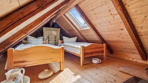 Een houten slaapkamer op zolder met twee bedden, een kaptafel en een dakraam.