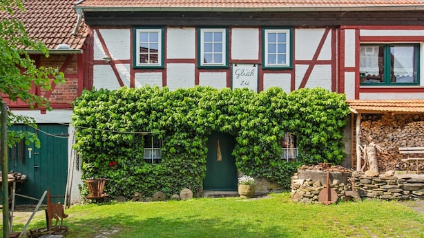 Een traditioneel vakwerkhuis met een groene muur begroeid met klimop, een zichtbaar bord en een stenen muur met houtblokken.