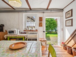 A rustic kitchen with a wooden table, a microwave, and a stove. There is a window with a view of a garden and a door leading outside. - Rustic home near farmhouse in the South Harz (Sangerhausen)