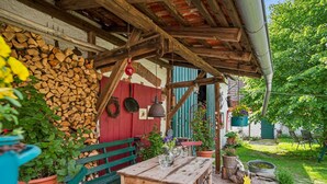 Een rustieke buitenzitplaats met een houten tafel en banken, omgeven door potplanten en een stapel hout.