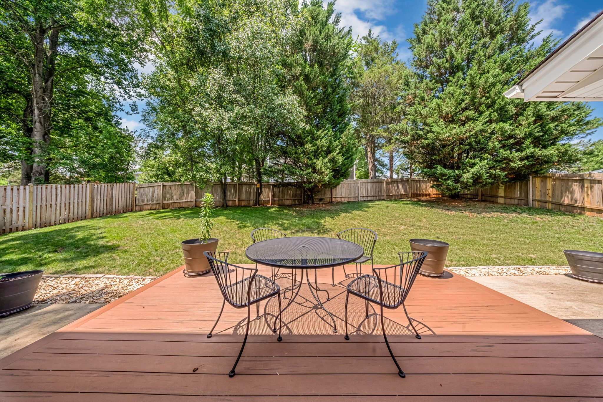 Een terras met een ronde tafel en stoelen, omringd door een houten vlonder en een houten hek.