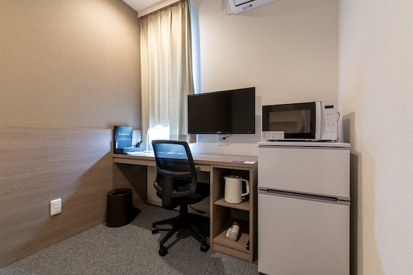 A hotel room with a desk, a flat-screen TV, a microwave, a coffee maker, and a mini-fridge.