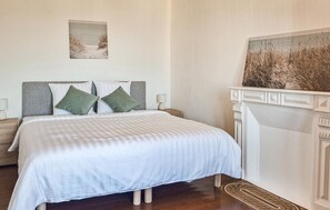 Une chambre à coucher comprenant un lit, des tables de chevet, une cheminée et deux tableaux accrochés au mur.