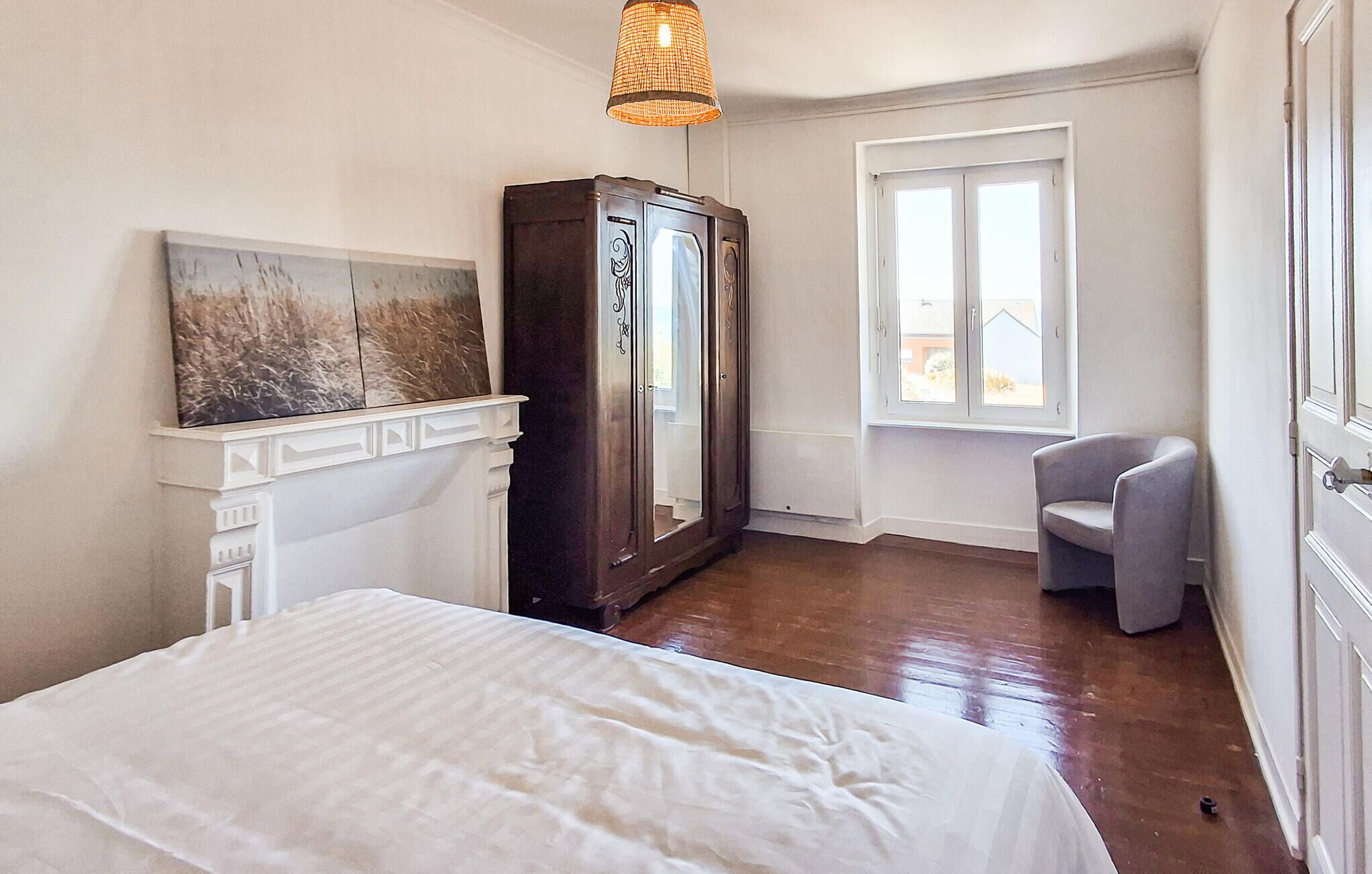 A bedroom with a bed, a wardrobe, a chair, a window, and a painting on the wall.