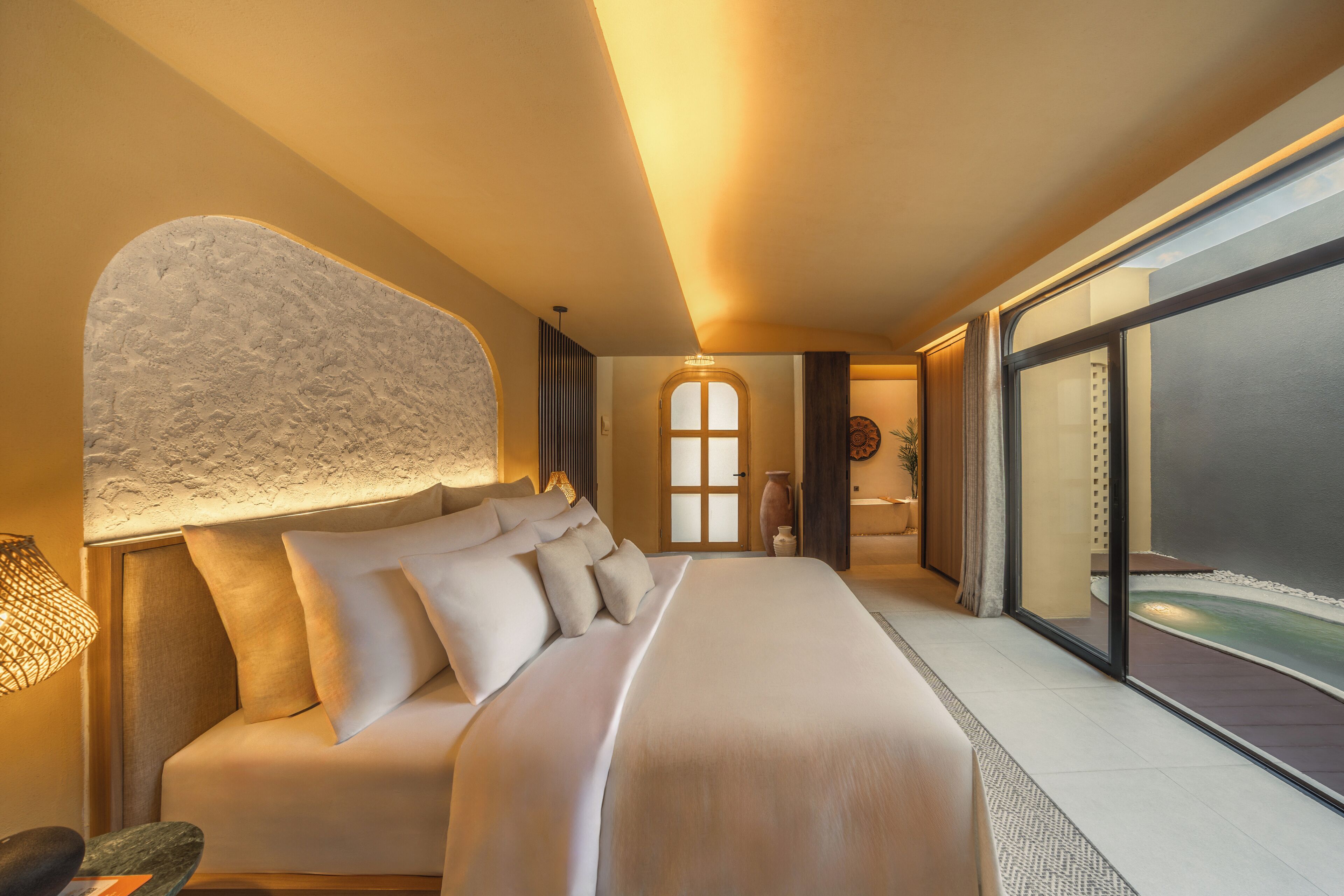 Habitación de hotel moderna con una cama grande, vista al océano y una pared con textura original.