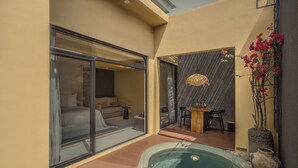 Et spa-område med jacuzzi, et opholdsområde med bord og stole samt en glasdør, der fører til et soveværelse.