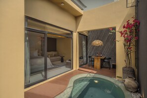 Uma área de spa com hidromassagem, espaço de estar com mesa e cadeiras, e porta de vidro que dá para um quarto.