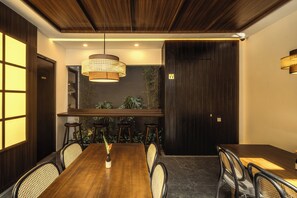 Sala de conferências com mesa de madeira, cadeiras, luminária pendente e planta na parede.