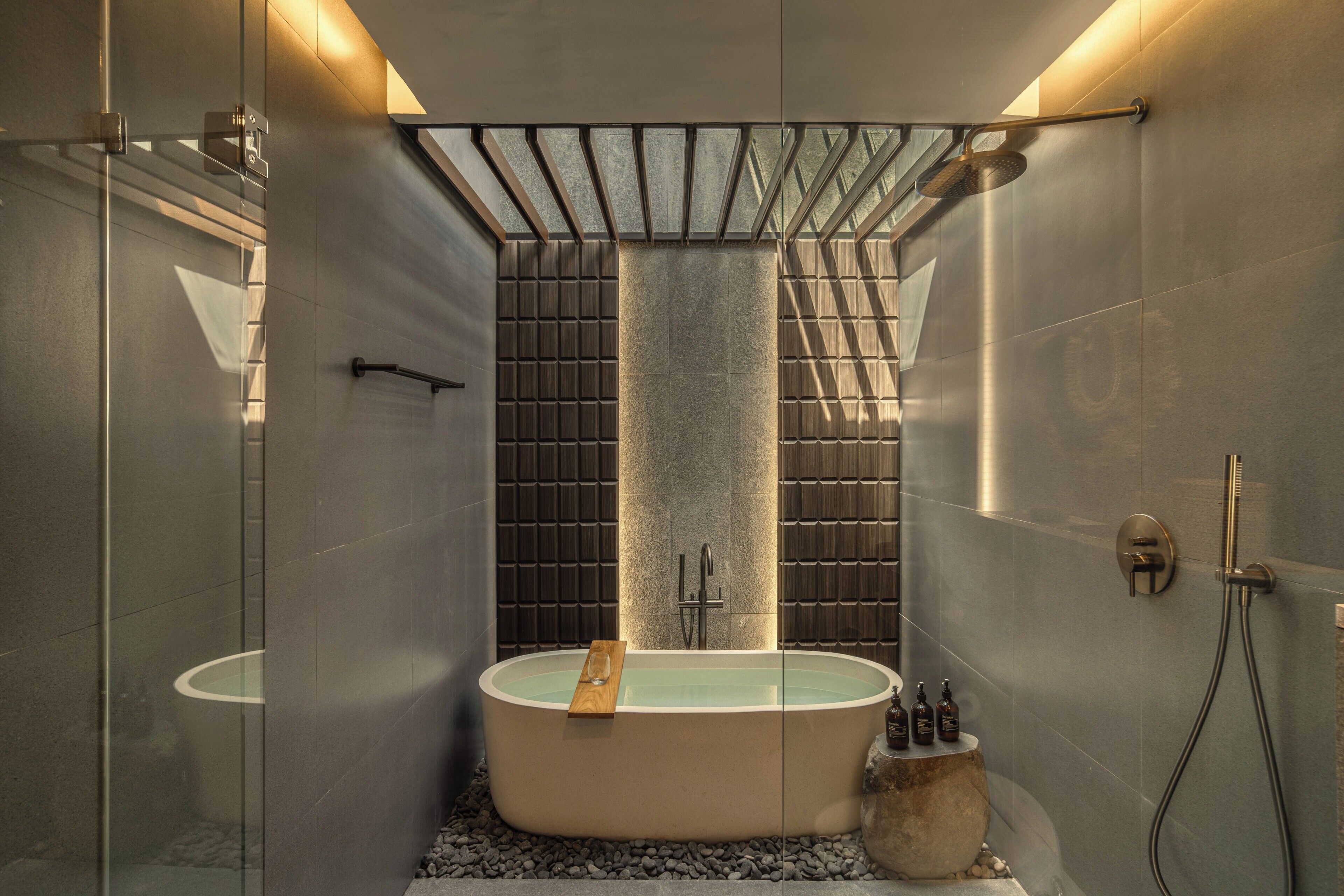 A modern bathroom with a freestanding bathtub, a glass shower enclosure, and a stone wall.