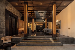 A hotel lobby with a staircase leading to a dining area, wooden beams on the ceiling, and a stone wall. - Leedon Villa Seminyak by Ini Vie Hospitality (Kuta Utara, Badung)