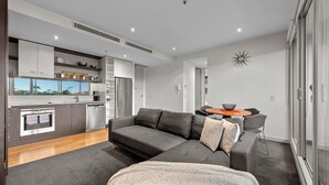 Een modern appartement met een grijze bank, een eettafel en een keuken met een inbouwoven en koelkast.