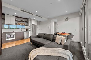 Ein modernes Apartment mit grauem Sofa, einem kleinen Esstisch und einer Küchenzeile mit Einbauofen und Kühlschrank.