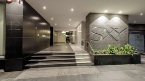 Een moderne gevel met een trap naar de lobby, een groot 'SX' bord en een brandmelder aan de muur.