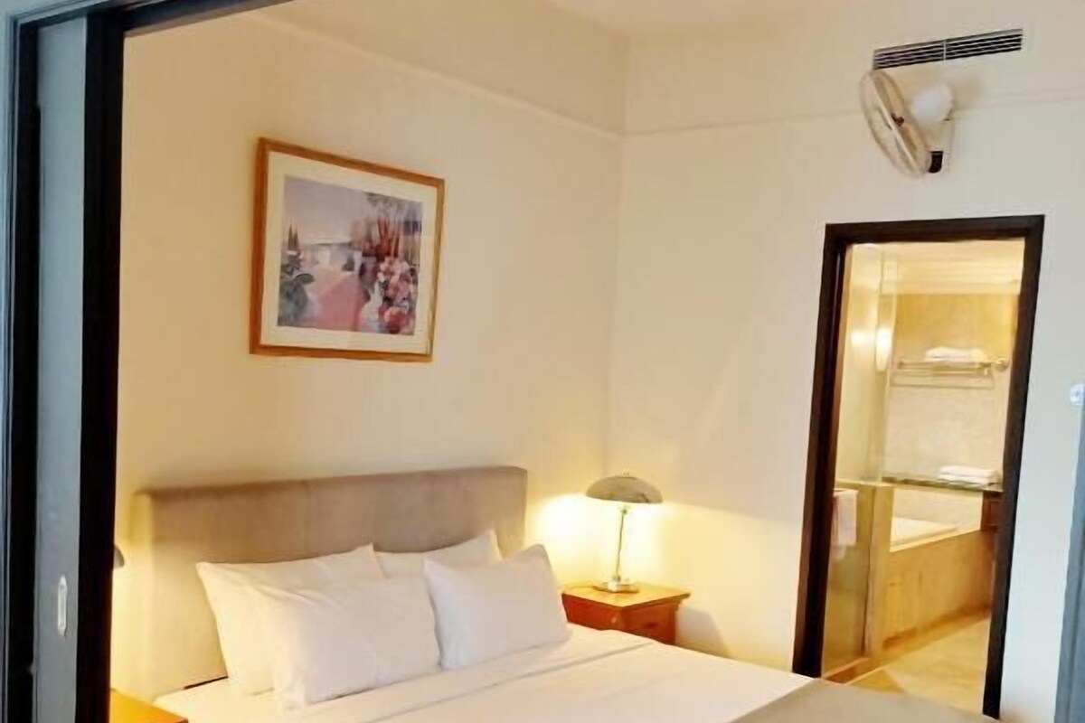 Ein Hotelzimmer mit Bett, Nachttisch, Lampe, einem gerahmten Bild an der Wand und einem durchgegangenen Tür sichtbaren Badezimmer.