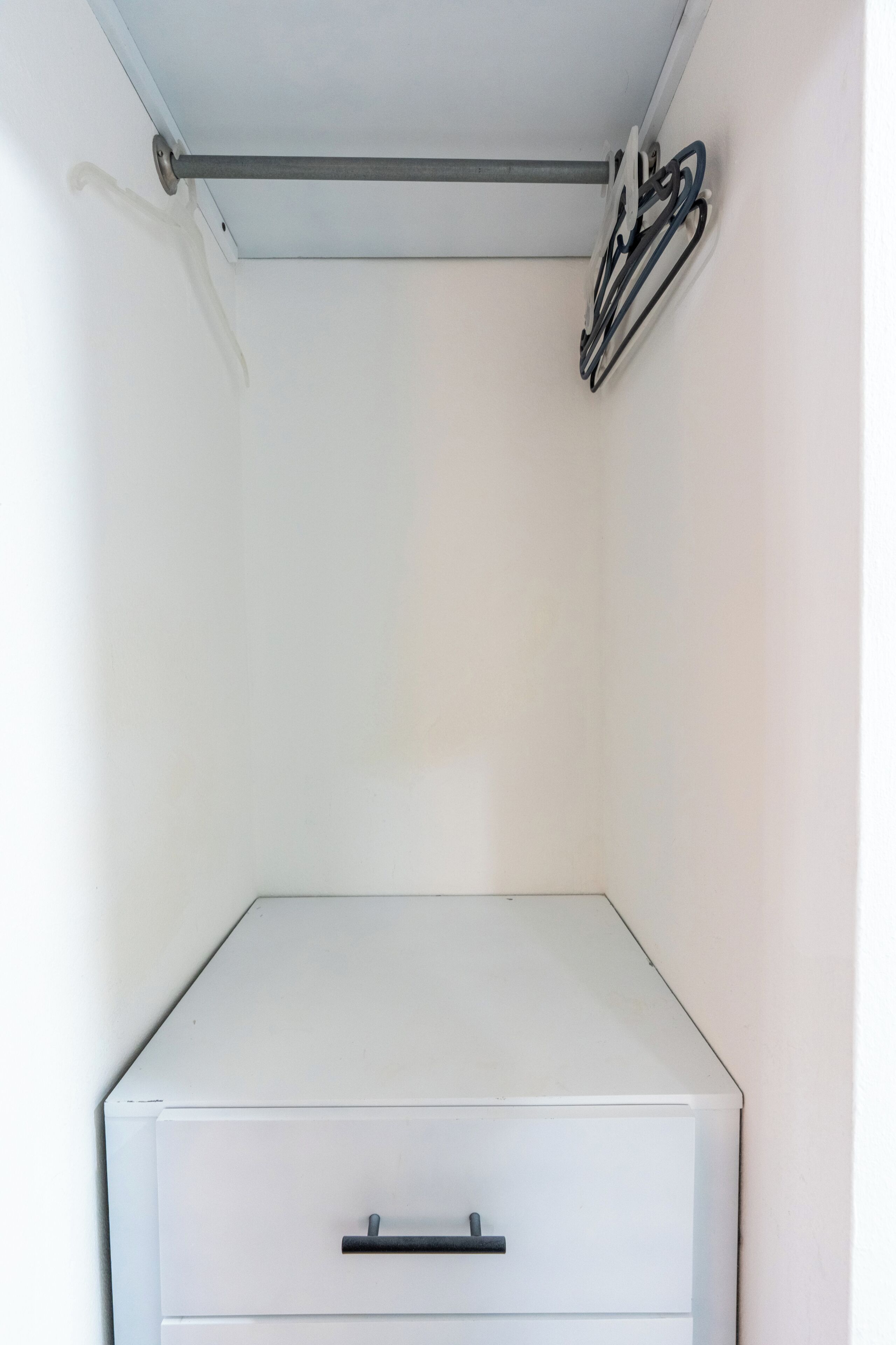 A white storage unit with a metal rod and black hangers.