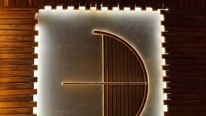 A metallic wall with a geometric design, possibly a logo or emblem, set against a wooden panel background. - Meghsomudro Eco Resort Sajek (Sajek)