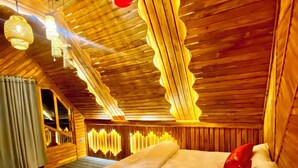 A room with a sloped ceiling, wooden walls, a bed with white bedding, and hanging light fixtures.