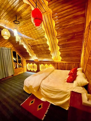 A room with a sloped ceiling, wooden walls, a bed with white bedding, and hanging light fixtures.