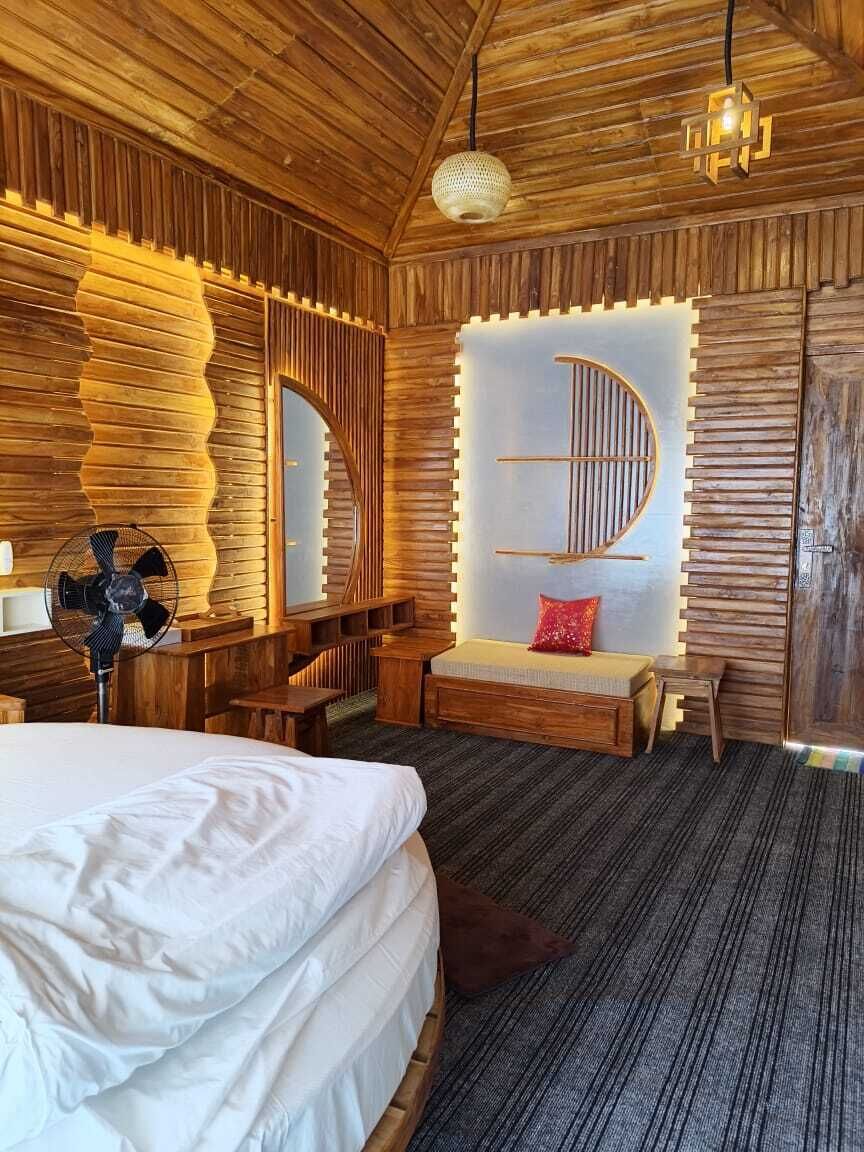 Ein Zimmer aus Holz mit einem Bett, einer Bank, einem Ventilator und einer Wandleuchte.