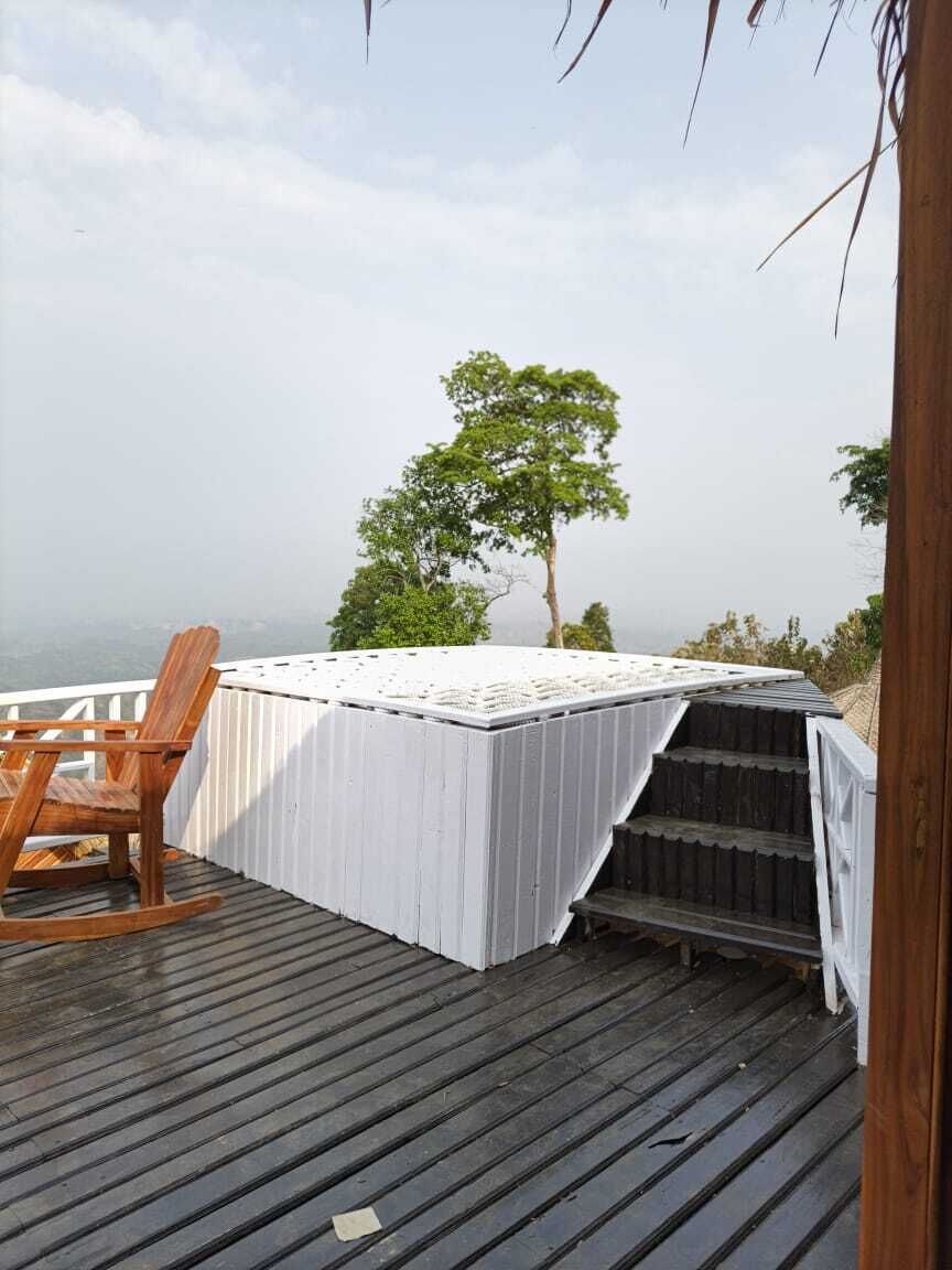 Um deck de madeira com área coberta branca, uma cadeira de balanço e vista para o oceano.