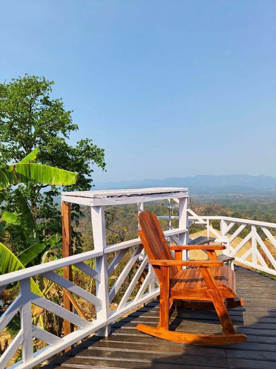 A wooden deck with a white railing, a rocking chair, and a small table.
