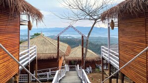 A wooden structure with a thatched roof, a staircase leading to a higher level, and a view of distant mountains. - Meghsomudro Eco Resort Sajek (Sajek)